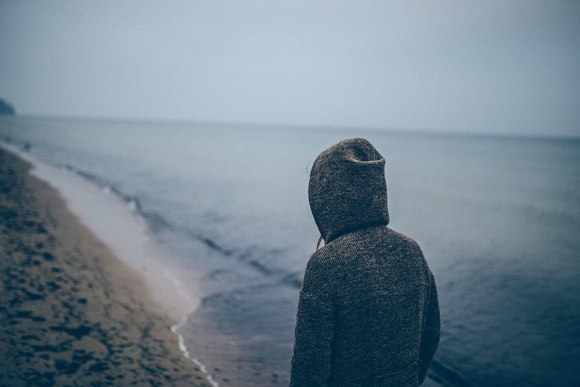 Individual standing by ocean with hoodie on. If you're experiencing symptoms of anxiety or trauma, talk with an online therapist who gets it. Anxiety and trauma in Detroit, MI have a greater connection than you realize. Call now and get support with anxiety counseling or trauma therapy!