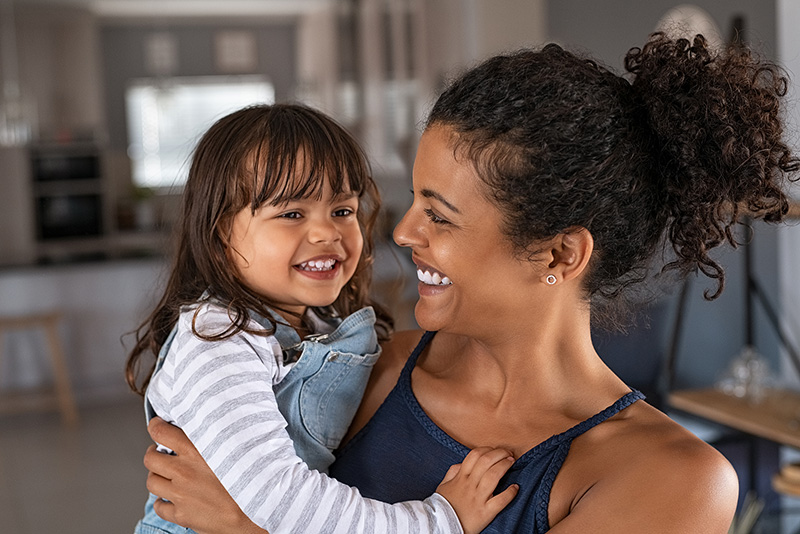 Mom holding daughter and smiling. If you're struggling to be present due to work, relationships or other tasks, get support with therapy for moms in Detroit, MI. No longer be an overwhelmed mom with the help of an online therapist. Additionally we provide therapy for new moms as well. 