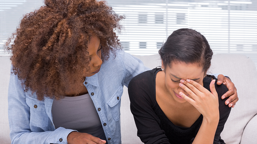 Woman sitting next to friend upset and being consoled. Often when we are dealing with perfectionist childhood trauma, anxiety and trauma, or depression and trauma, we are dealing with it alone. Get support from a trauma therapist in PTSD treatment and trauma therapy in Detroit, MI today!