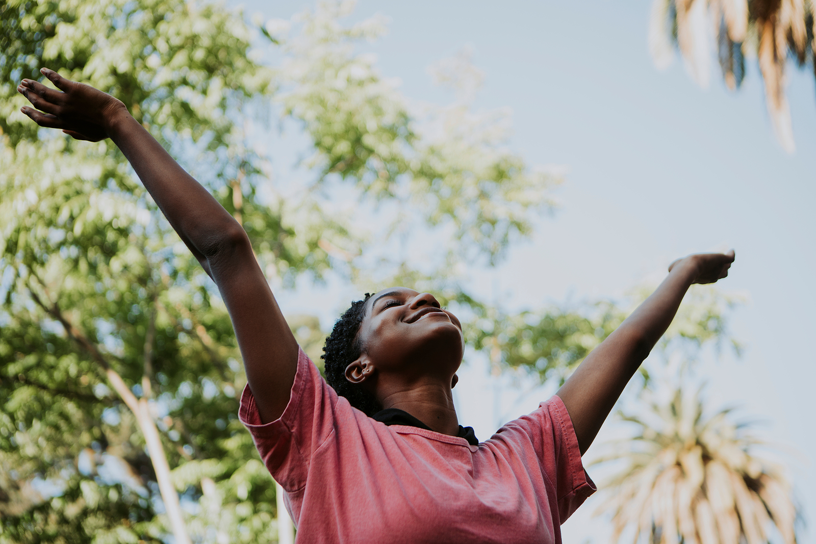 Woman in pink shirt raising hands up in air. Are you struggling to begin overcoming perfectionism in Detroit, MI? Begin therapy for anxiety and perfectionism today! Our online therapists are here to help!