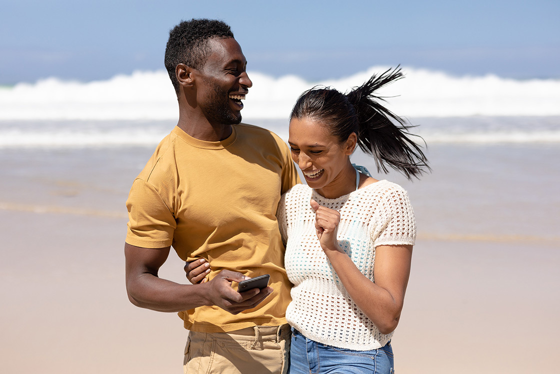Happy interracial couple holding each other and smiling at the beach. Our therapists are here to guide you toward better mental heath. Get the support you have been seeking in online therapy in Michigan today. We provide therapy for anxiety, trauma, perfectionism, couples, working professionals, and more. Call now!