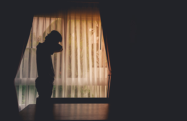 Man in dimly lit window with hands on neck in distress. If you're used to managing everyone else's health but yours, its time to focus on your men's mental health today. We offer therapy for men in detroit, mi for you!