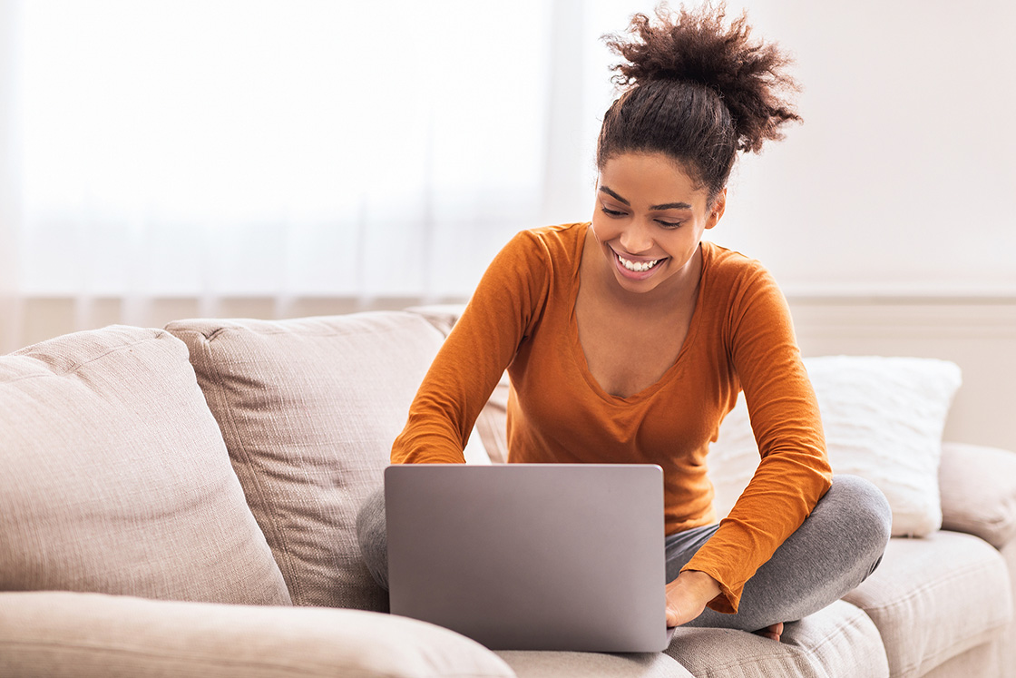 Woman on laptop smiling on couch. Our EMDR therapists know that EMDR for trauma and EMDR for anxiety can create a huge sense of relief. Why not see if EMDR therapy in Detroit, MI is for you? Call now and find relief with EMDR therapy near me today!